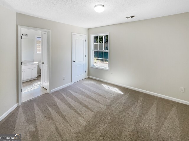 unfurnished bedroom featuring connected bathroom, light carpet, and multiple windows