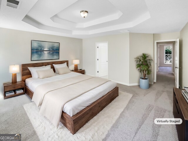 bedroom featuring light colored carpet and a raised ceiling