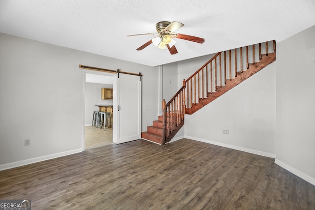 unfurnished living room featuring a textured ceiling, a barn door, ceiling fan, and dark hardwood / wood-style flooring