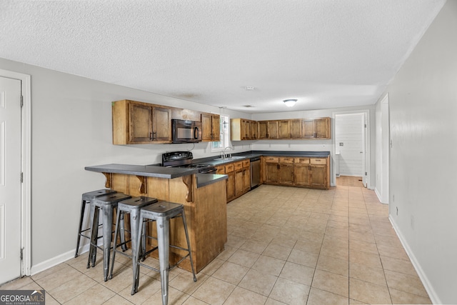 kitchen with black appliances, a kitchen bar, a textured ceiling, kitchen peninsula, and light tile patterned floors