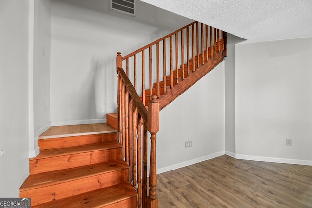 staircase with a textured ceiling and wood-type flooring