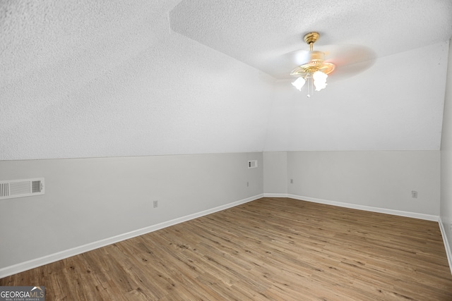 additional living space with vaulted ceiling, a textured ceiling, light hardwood / wood-style flooring, and ceiling fan