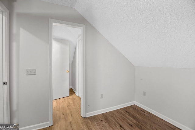 bonus room with vaulted ceiling, light hardwood / wood-style flooring, and a textured ceiling