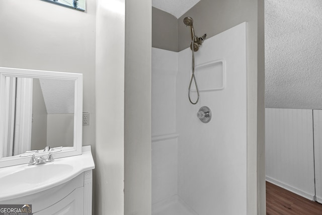 bathroom featuring a textured ceiling, walk in shower, wood-type flooring, vaulted ceiling, and vanity