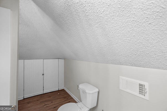 bathroom with hardwood / wood-style floors, vaulted ceiling, a textured ceiling, and toilet