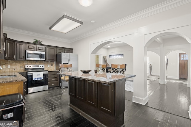 kitchen featuring sink, light stone counters, appliances with stainless steel finishes, a kitchen island, and decorative backsplash