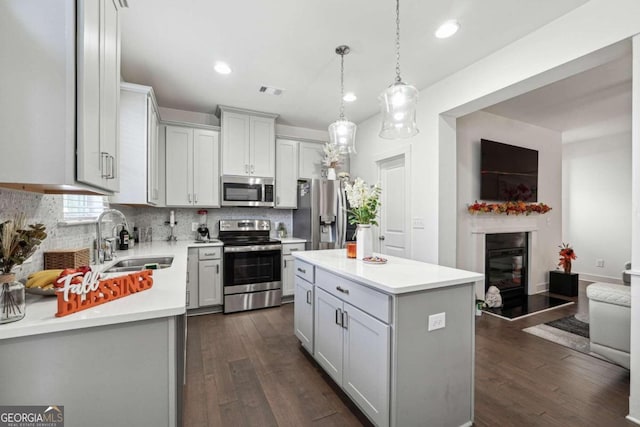 kitchen with appliances with stainless steel finishes, sink, a kitchen island, pendant lighting, and dark wood-type flooring