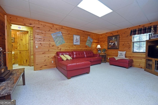 living room with a drop ceiling, wood walls, and carpet