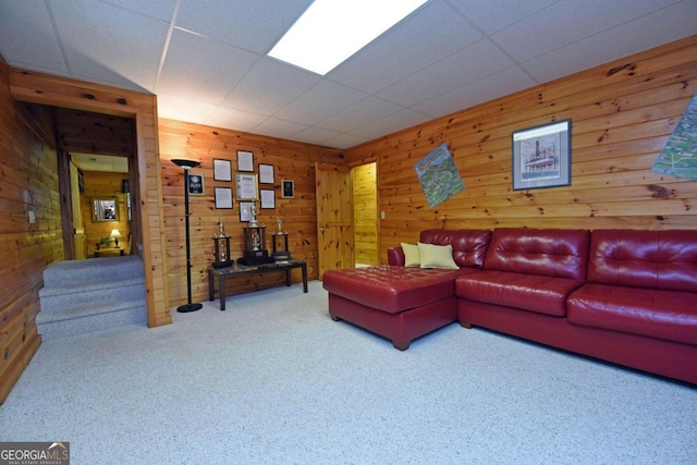 carpeted living room with a drop ceiling and wooden walls