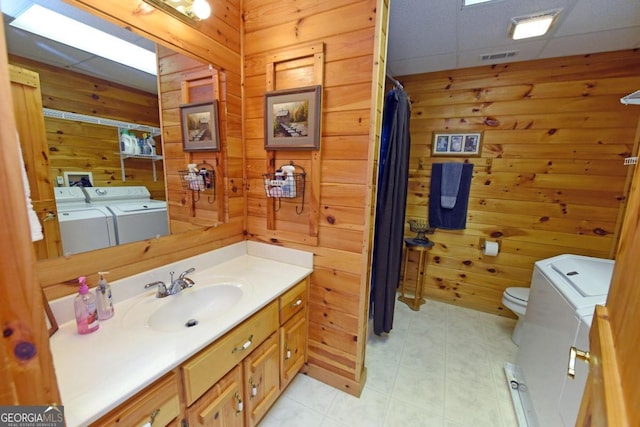 bathroom with washing machine and dryer, a drop ceiling, toilet, wooden walls, and vanity