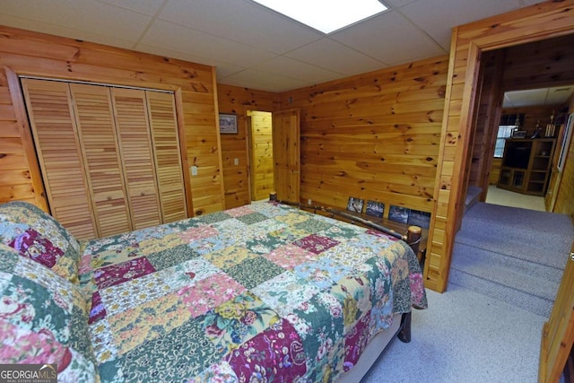 carpeted bedroom featuring a closet, wood walls, and a paneled ceiling