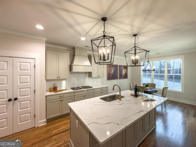 kitchen featuring stainless steel appliances, sink, decorative light fixtures, a kitchen island with sink, and premium range hood