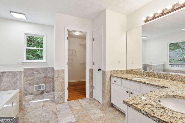 bathroom featuring tile walls, vanity, independent shower and bath, and a textured ceiling