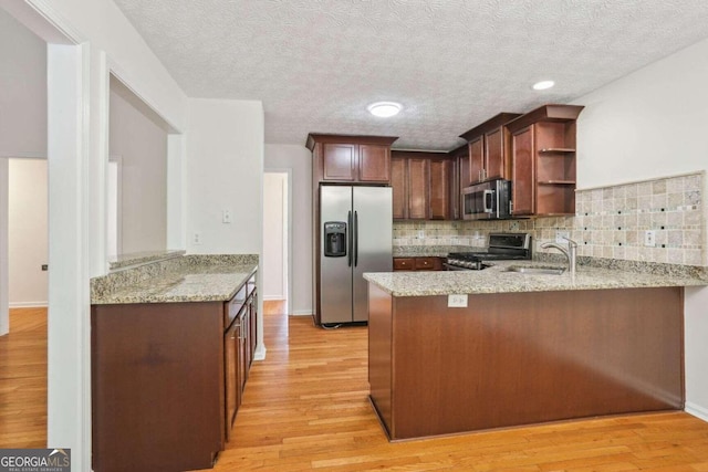 kitchen with stainless steel appliances, light stone countertops, light hardwood / wood-style flooring, and kitchen peninsula