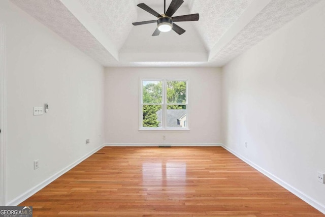 spare room featuring light hardwood / wood-style floors, a textured ceiling, a tray ceiling, and ceiling fan