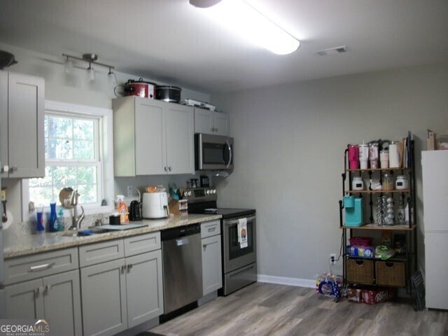 kitchen with sink, light stone countertops, stainless steel appliances, and light wood-type flooring