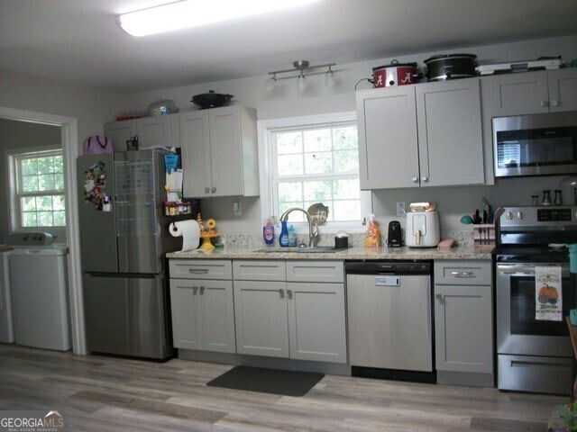 kitchen with washer / dryer, appliances with stainless steel finishes, sink, and light wood-type flooring