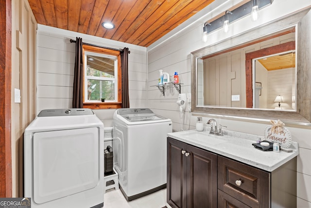 clothes washing area featuring cabinets, sink, independent washer and dryer, wood ceiling, and wooden walls