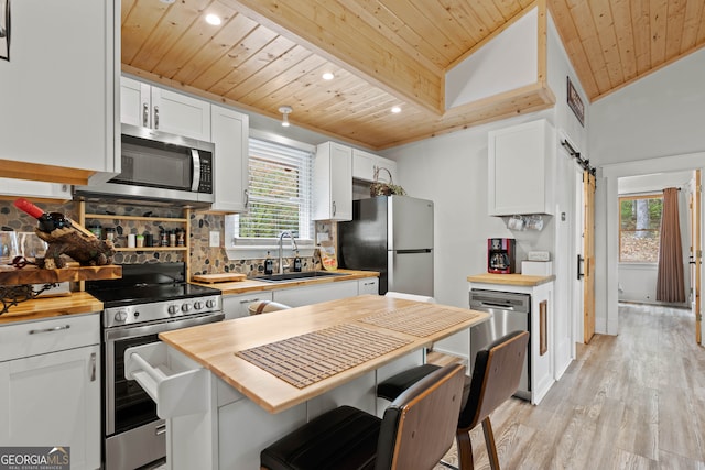 kitchen with stainless steel appliances, white cabinetry, wooden counters, lofted ceiling, and a barn door