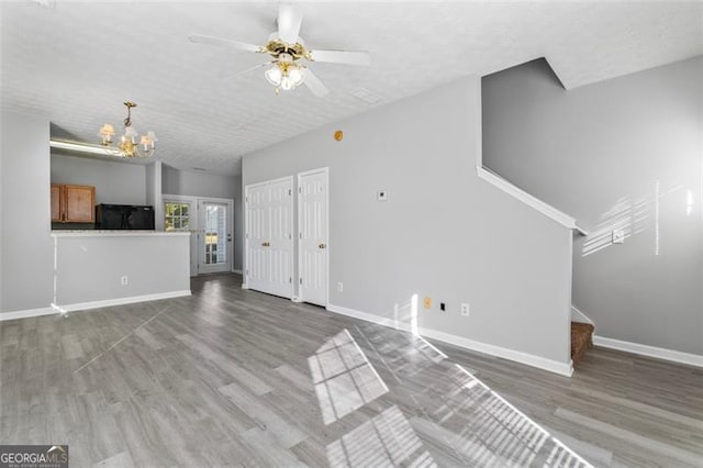 unfurnished living room featuring a textured ceiling, wood-type flooring, and ceiling fan with notable chandelier