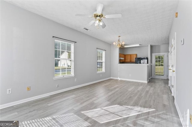 unfurnished living room featuring a wealth of natural light, a textured ceiling, ceiling fan with notable chandelier, and light wood-type flooring