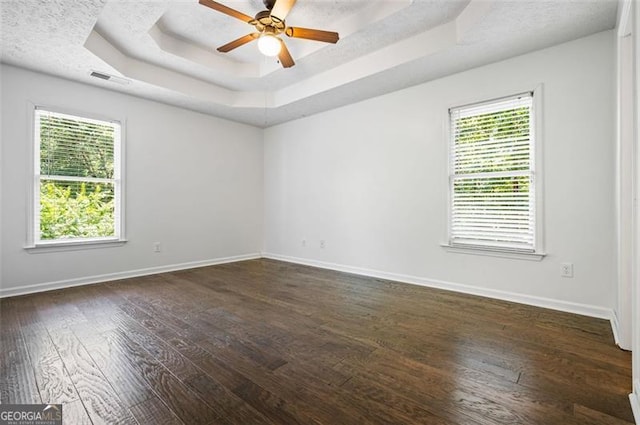 unfurnished room featuring a wealth of natural light, dark wood-type flooring, and a tray ceiling