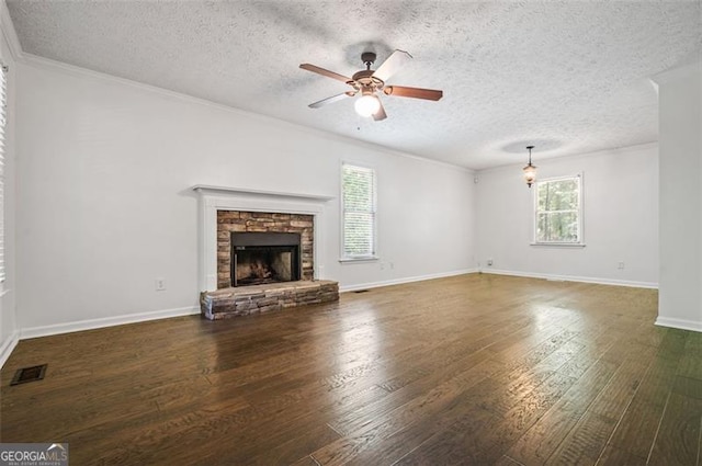 unfurnished living room with ceiling fan, a textured ceiling, dark hardwood / wood-style floors, a stone fireplace, and crown molding