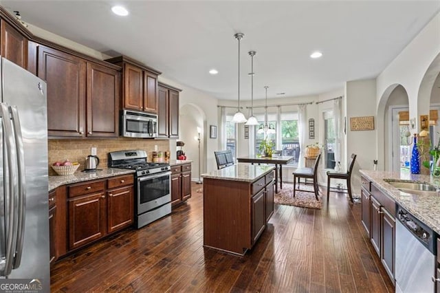 kitchen with appliances with stainless steel finishes, a kitchen island, decorative light fixtures, light stone counters, and dark hardwood / wood-style floors