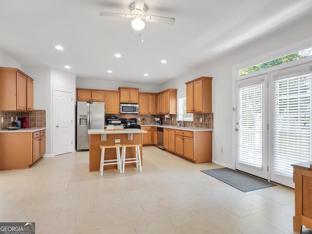 kitchen featuring stainless steel appliances, a kitchen island, a breakfast bar area, ceiling fan, and sink