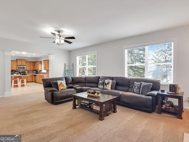 carpeted living room with ceiling fan, ornate columns, and sink