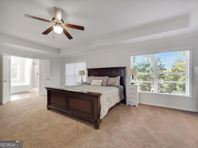 bedroom with light colored carpet, ceiling fan, a tray ceiling, and connected bathroom