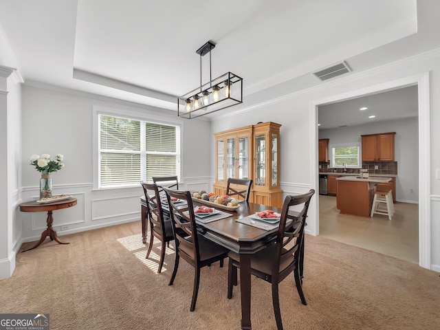 dining area with sink, a raised ceiling, light carpet, and plenty of natural light