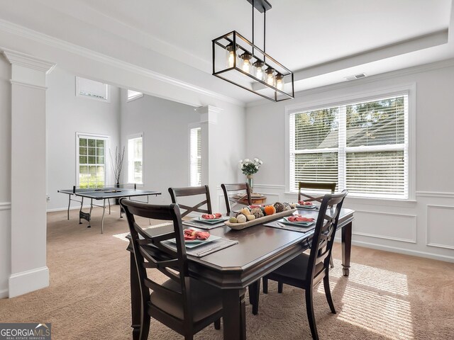 carpeted dining room featuring a notable chandelier, a raised ceiling, and ornate columns