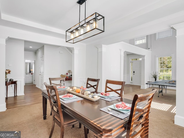 carpeted dining area featuring decorative columns, ornamental molding, and a chandelier