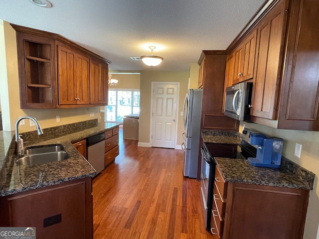 kitchen with appliances with stainless steel finishes, sink, a textured ceiling, dark stone counters, and dark wood-type flooring