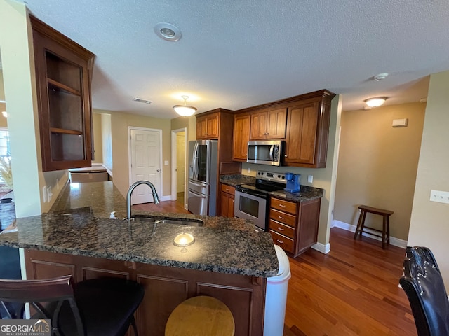 kitchen featuring dark hardwood / wood-style floors, kitchen peninsula, stainless steel appliances, sink, and a textured ceiling