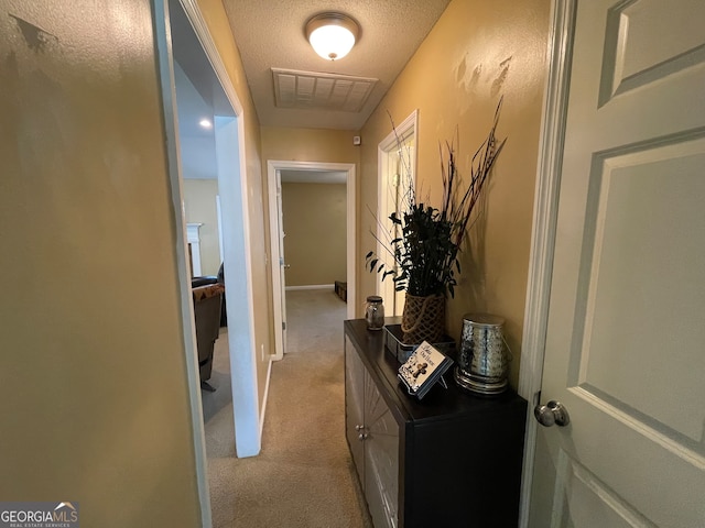 hallway with light carpet and a textured ceiling