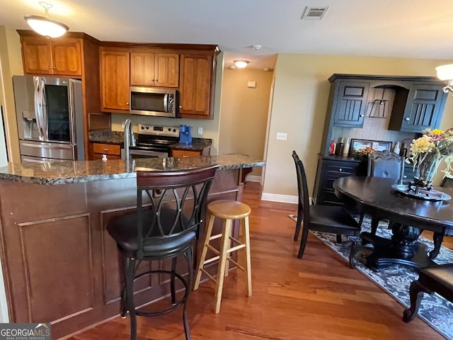 kitchen featuring a breakfast bar area, dark wood-type flooring, appliances with stainless steel finishes, and dark stone counters