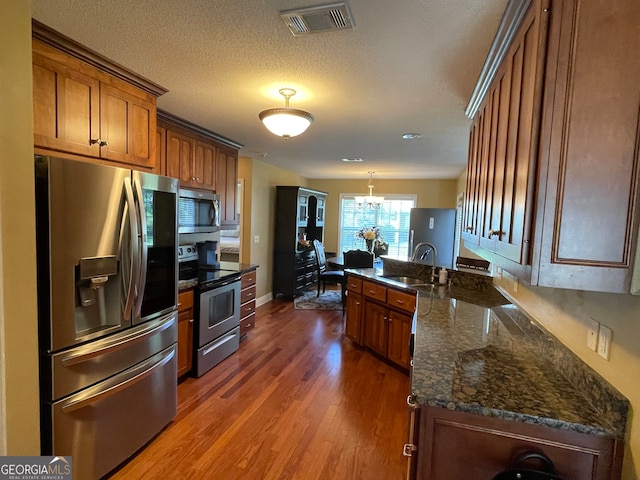 kitchen with dark hardwood / wood-style floors, kitchen peninsula, sink, decorative light fixtures, and appliances with stainless steel finishes