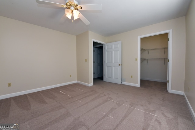 unfurnished bedroom with a closet, light colored carpet, a walk in closet, and ceiling fan