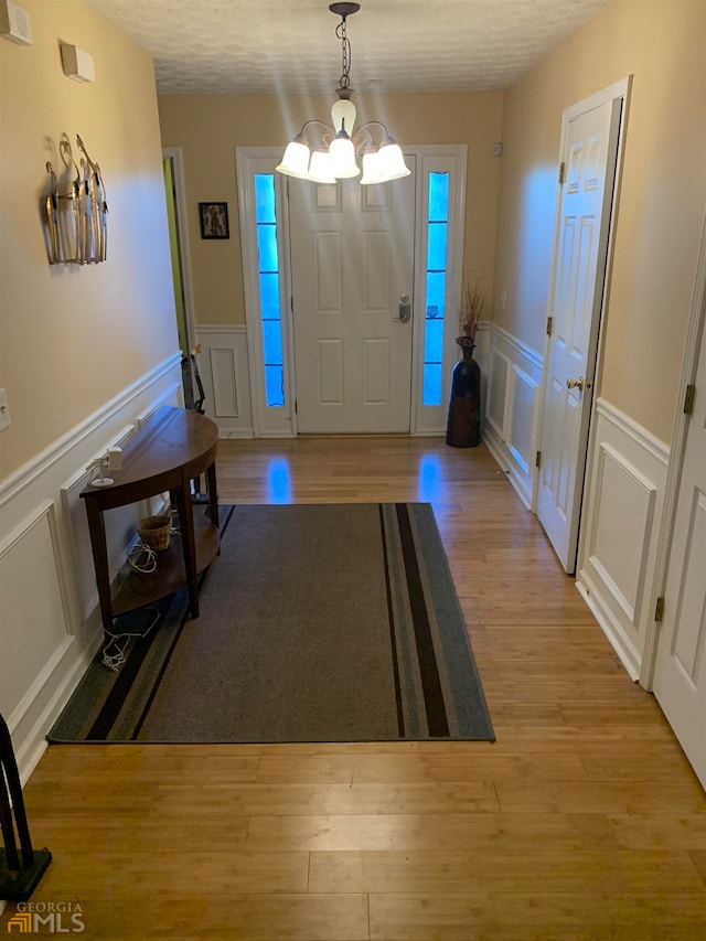 foyer entrance with an inviting chandelier, a textured ceiling, and light wood-type flooring