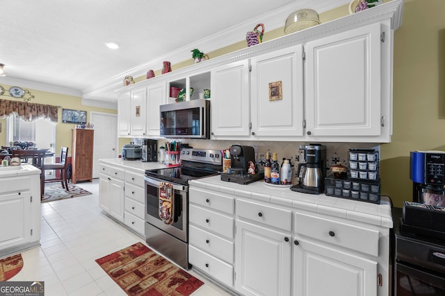 kitchen with crown molding, appliances with stainless steel finishes, tile counters, and white cabinets