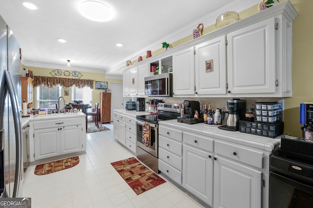 kitchen with decorative backsplash, tile counters, stainless steel appliances, crown molding, and white cabinetry