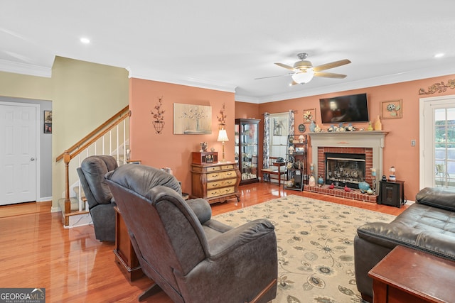 living room featuring crown molding, a fireplace, light wood-type flooring, and ceiling fan