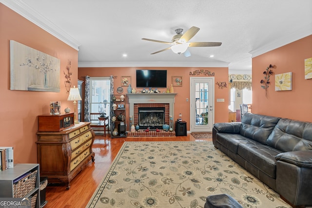 living room featuring crown molding, hardwood / wood-style flooring, ceiling fan, and a brick fireplace