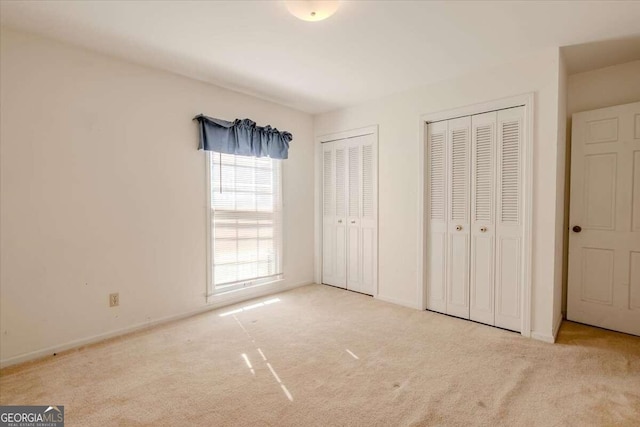 unfurnished bedroom with light carpet and multiple closets