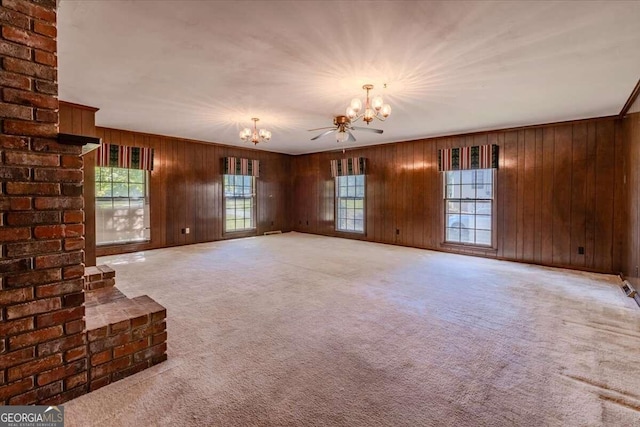 unfurnished living room with carpet flooring, a wealth of natural light, wooden walls, and ceiling fan with notable chandelier