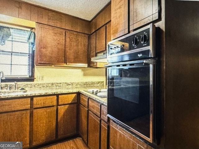 kitchen with black electric cooktop, sink, light stone counters, a textured ceiling, and light hardwood / wood-style floors