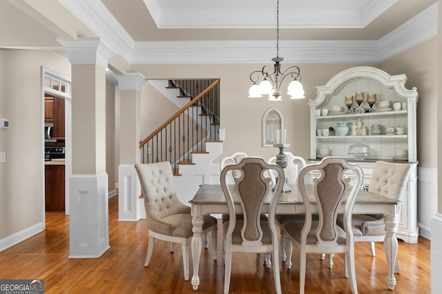 dining room with an inviting chandelier, a raised ceiling, decorative columns, light hardwood / wood-style floors, and ornamental molding