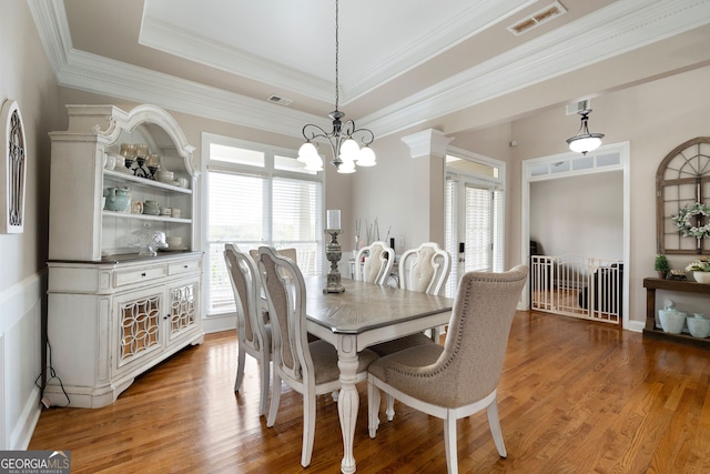 dining area featuring a raised ceiling, plenty of natural light, wood-type flooring, and an inviting chandelier